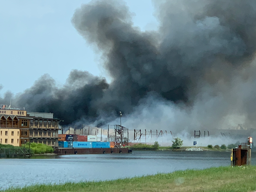 Eine Rauchsäule steigt über brennenden Lagerhallen auf